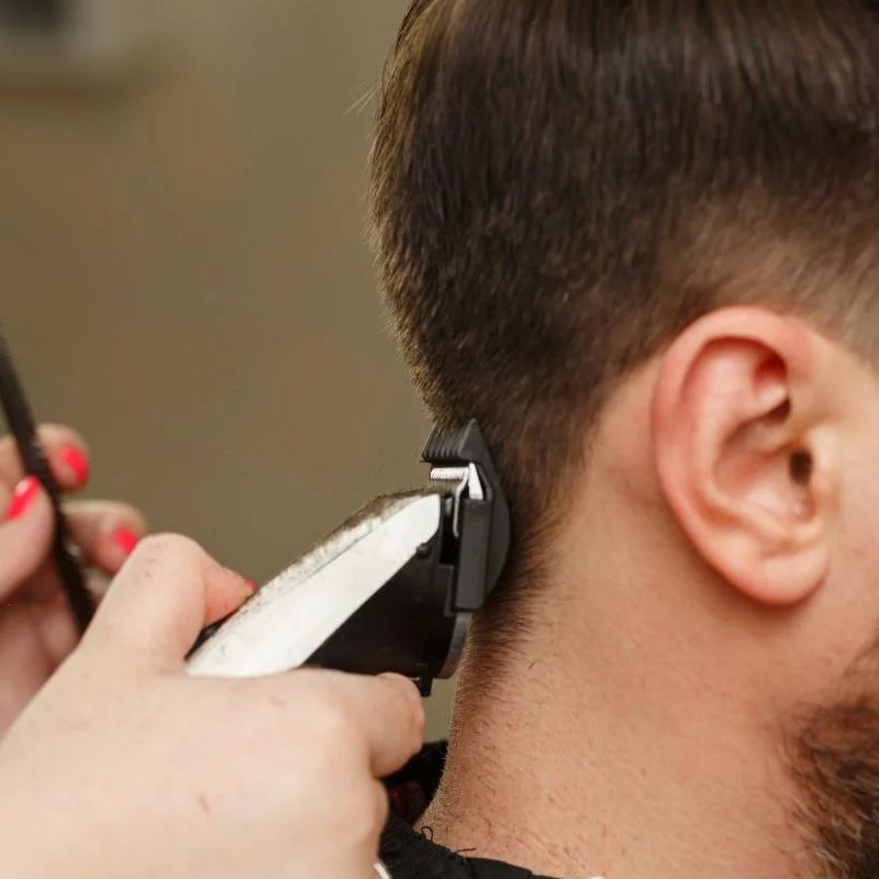 Peluquera cortándole el pelo a un hombre con una maquinilla